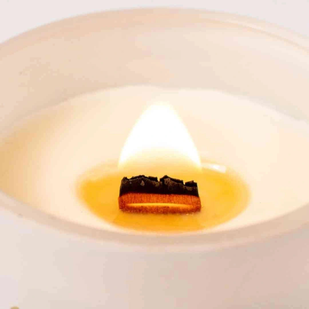 Close-up view of a wooden wick burning inside a white soy candle