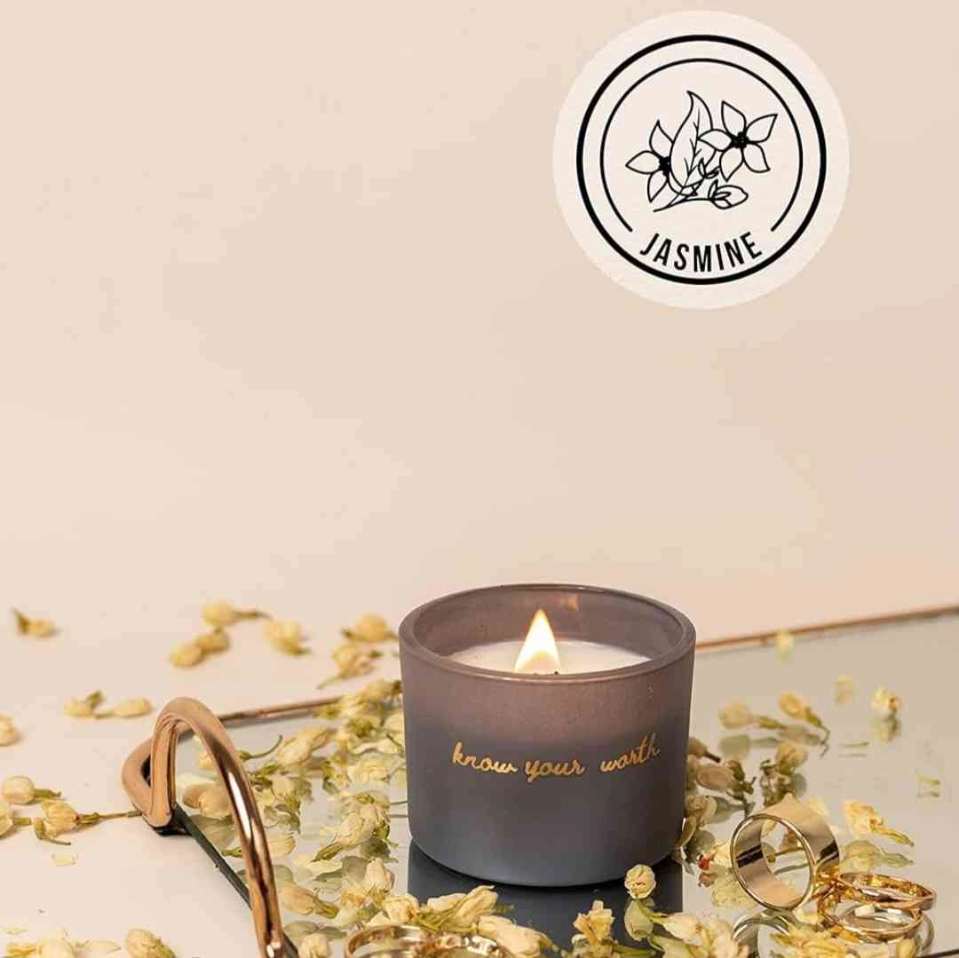 Gray candle with 'Know Your Worth' inscription, surrounded by jasmine flowers and displayed on a reflective surface, emphasizing its jasmine fragrance.