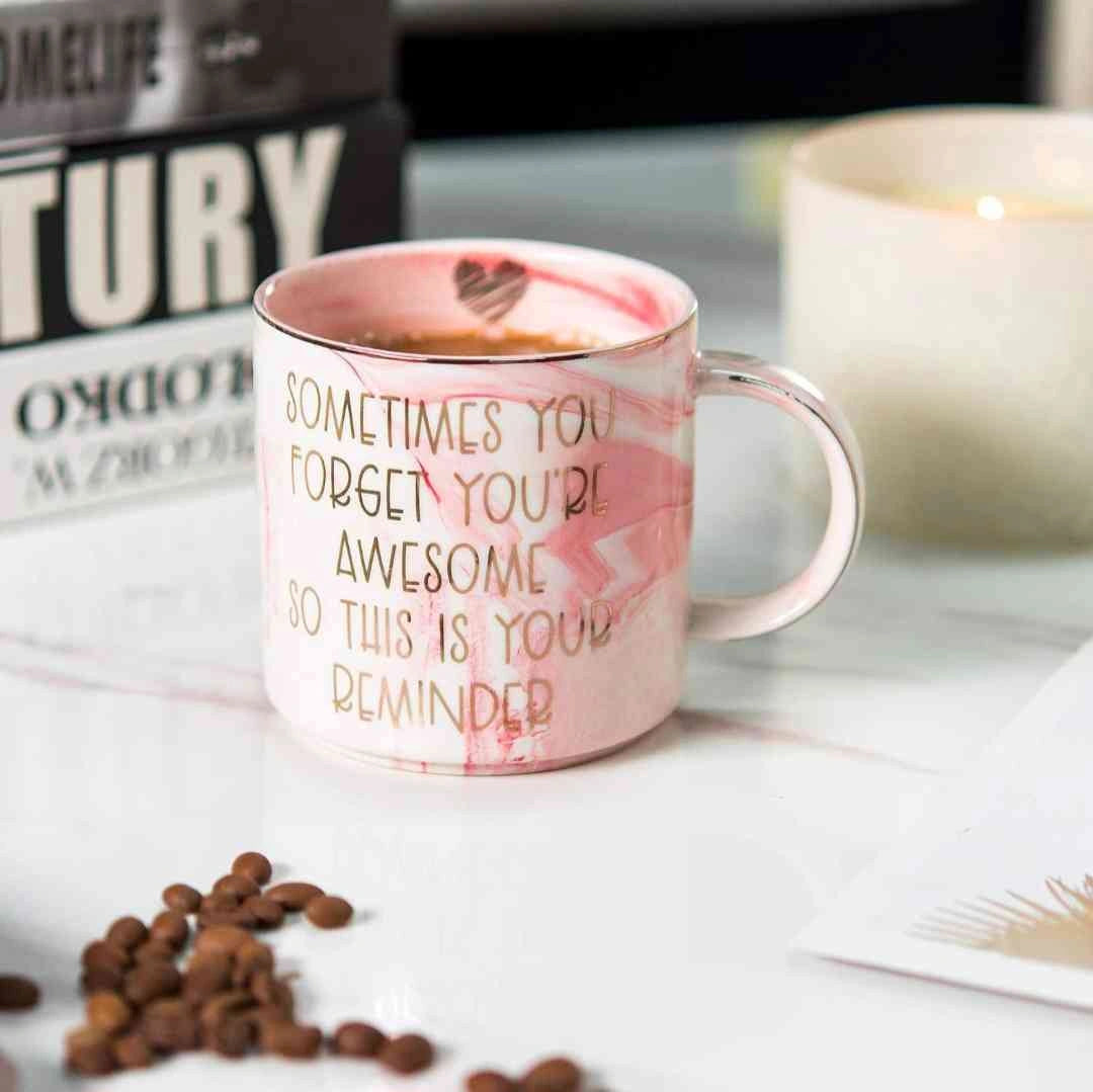 Pink marble coffee mug with motivational quote surrounded by coffee beans on a table