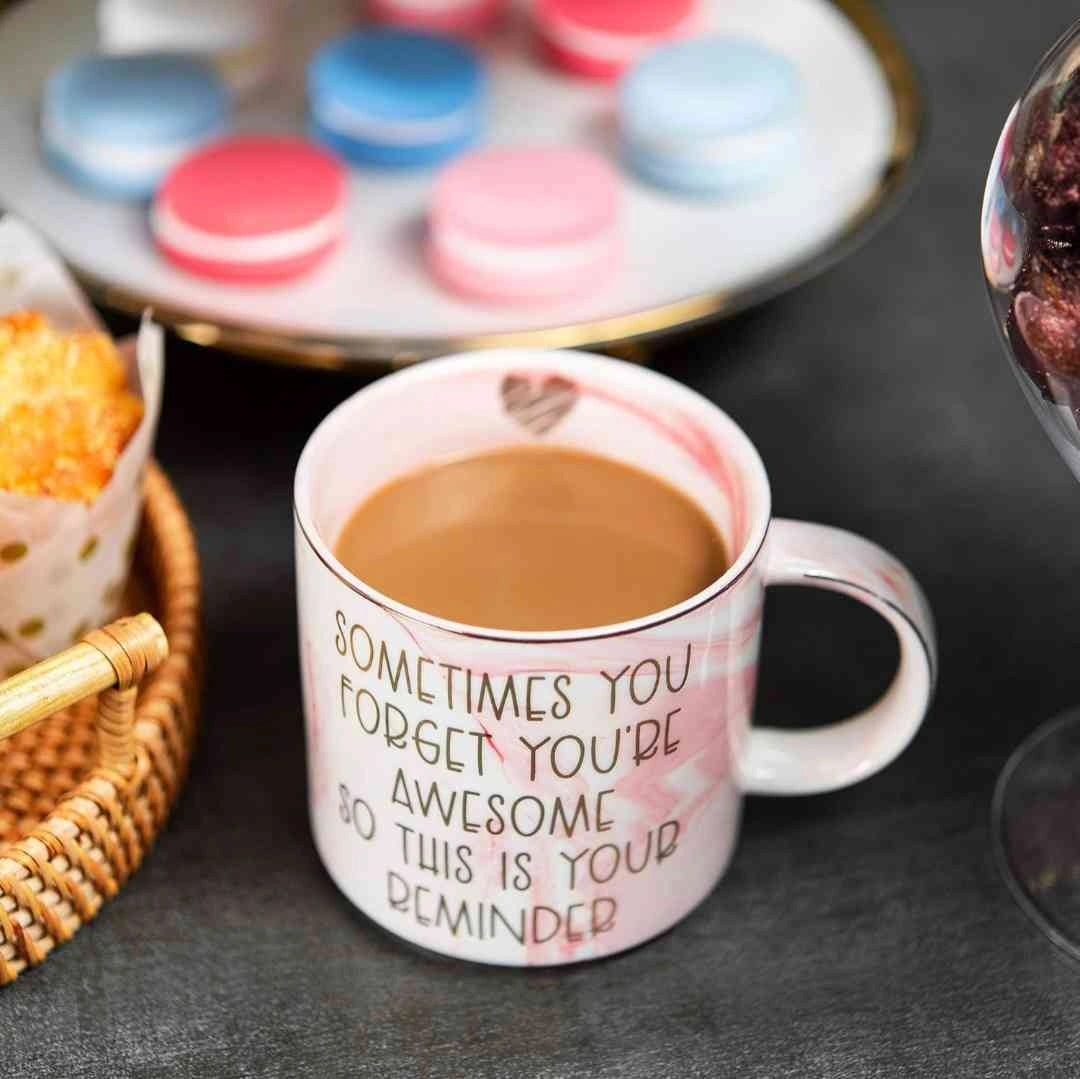 Pink marble mug with inspirational quote next to desserts and macarons on a table setting