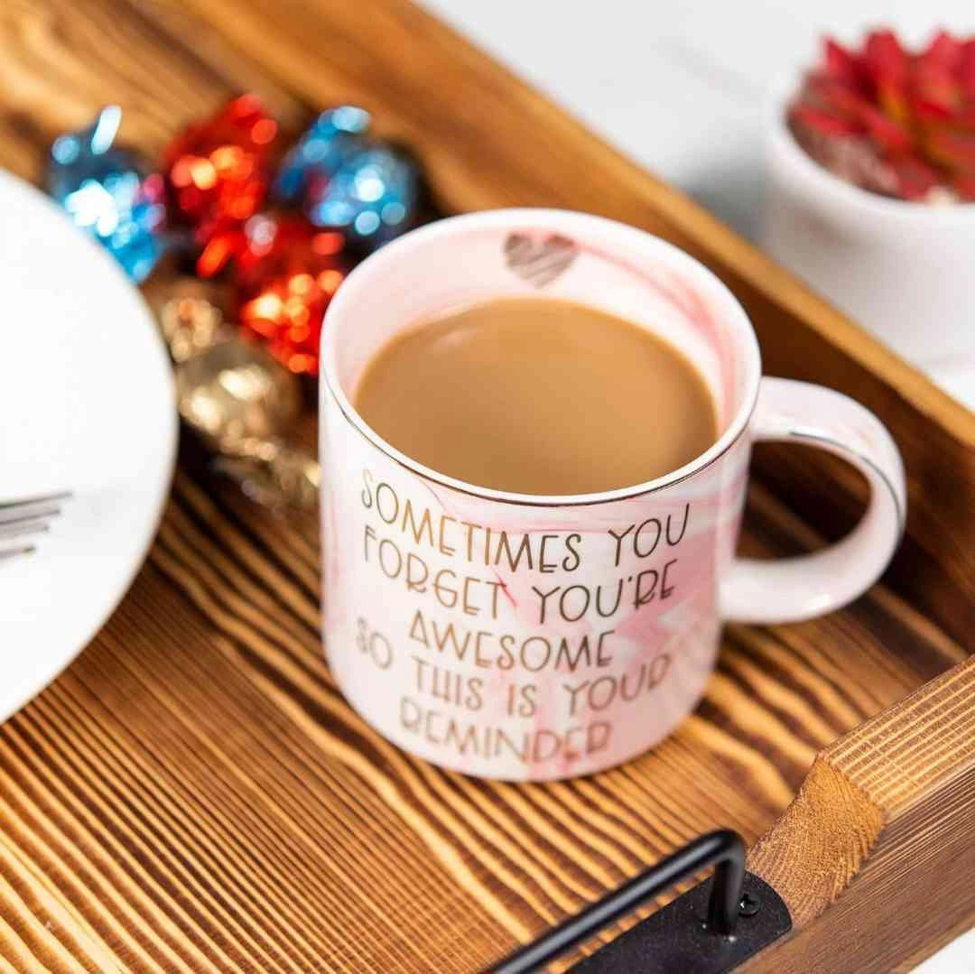 Pink coffee mug with motivational quote "Sometimes You Forget You’re Awesome" on a wooden tray