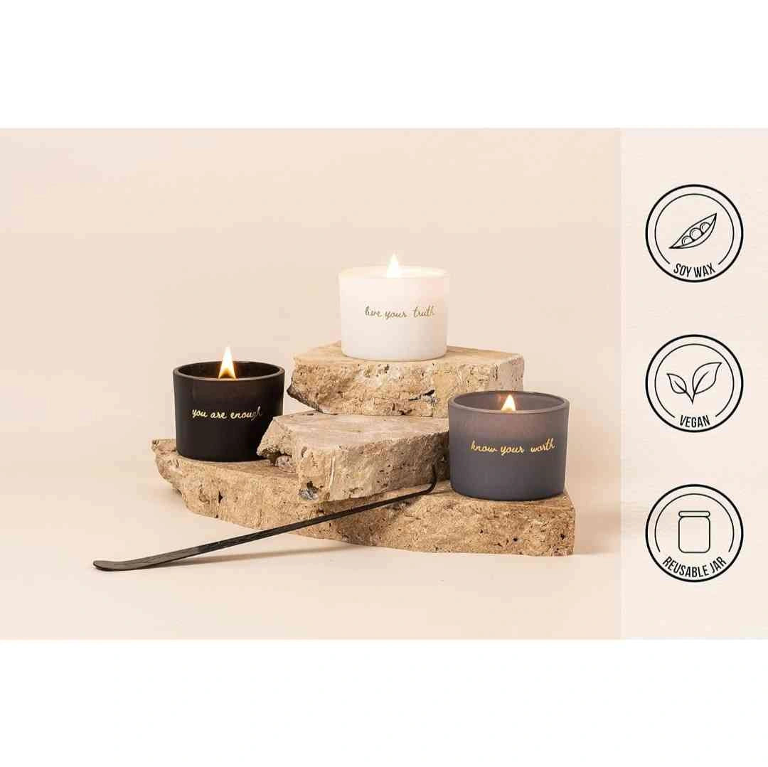 Three motivational candles in black, gray, and white jars, displayed with a focus on their sustainable features like soy wax, vegan ingredients, and reusable jars.